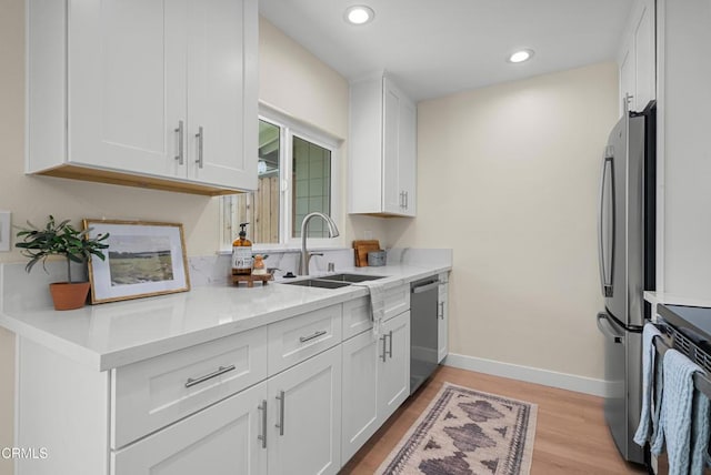 kitchen featuring stainless steel appliances, light wood-type flooring, white cabinetry, and a sink