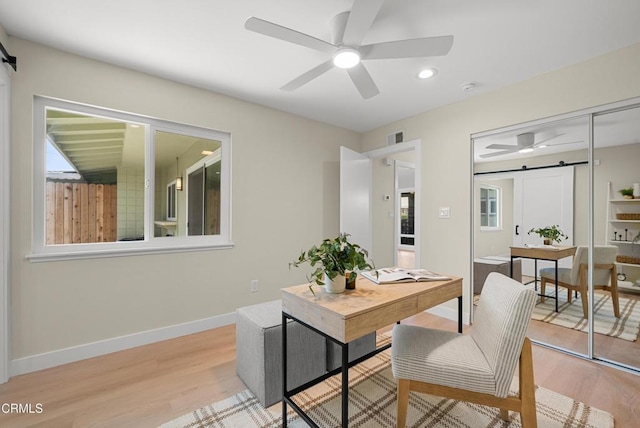 home office with visible vents, ceiling fan, light wood finished floors, and a barn door