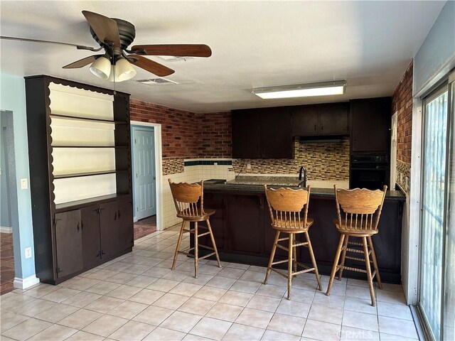 878 E Holly St, Rialto, CA 92376 - kitchen with black oven, a breakfast bar, brick wall, ceiling fan, and under cabinet range hood