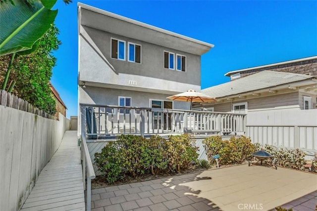 rear view of property featuring a deck, stucco siding, fence, and a patio area