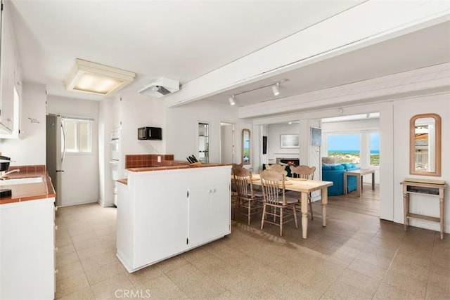 kitchen featuring tile countertops, white cabinetry, open floor plan, and light floors