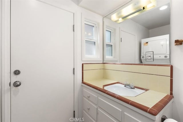 bathroom with stacked washer / drying machine, vanity, and decorative backsplash