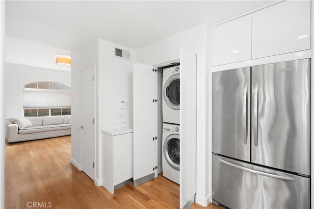 laundry area with visible vents, light wood-style floors, stacked washing maching and dryer, and laundry area