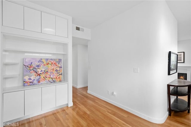 interior space with a lit fireplace, built in features, baseboards, visible vents, and light wood-style floors