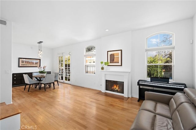 living room featuring a fireplace with flush hearth, baseboards, a chandelier, visible vents, and light wood-style flooring
