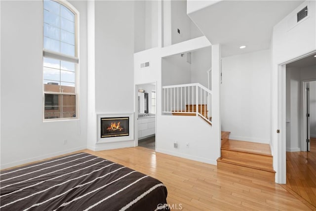 unfurnished bedroom featuring visible vents, hardwood / wood-style flooring, baseboards, a glass covered fireplace, and a high ceiling