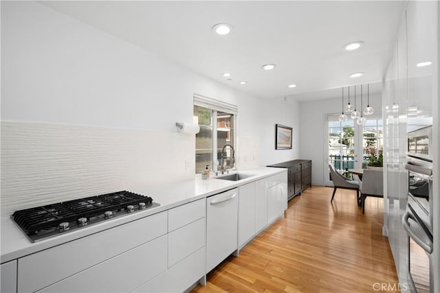 kitchen featuring white cabinets, light wood finished floors, modern cabinets, stainless steel appliances, and a sink