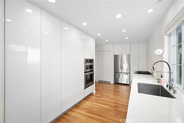 kitchen featuring modern cabinets, appliances with stainless steel finishes, white cabinetry, a sink, and light wood-type flooring
