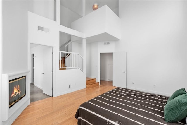 bedroom with baseboards, visible vents, a high ceiling, and wood finished floors