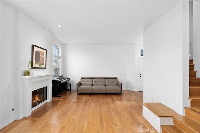 unfurnished room with stairway, recessed lighting, baseboards, light wood finished floors, and a glass covered fireplace