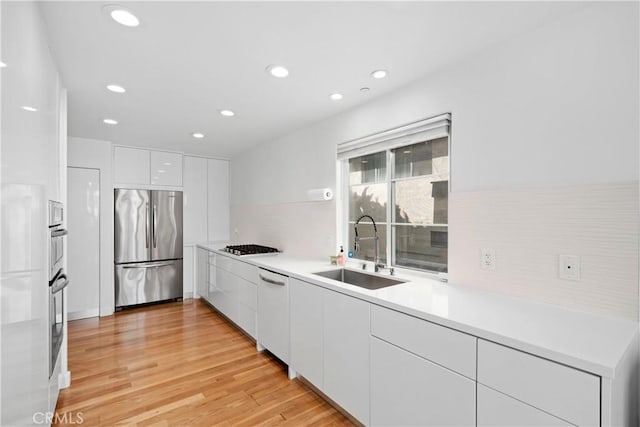 kitchen featuring white cabinets, dishwasher, modern cabinets, a sink, and freestanding refrigerator