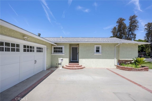 single story home with a garage, roof with shingles, and stucco siding