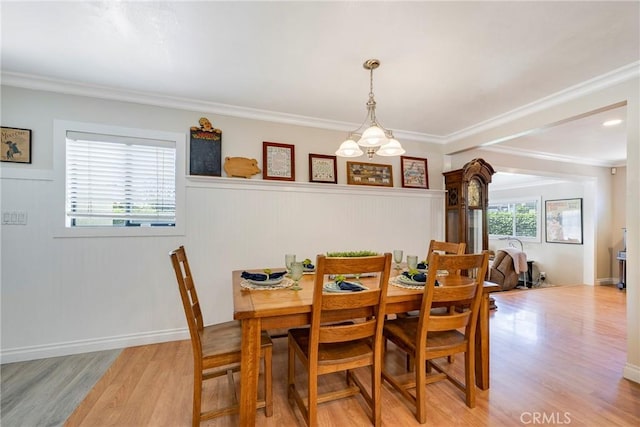 dining room with light wood-type flooring, crown molding, and wainscoting