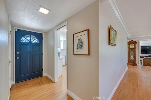 foyer featuring light wood finished floors, baseboards, and a textured ceiling