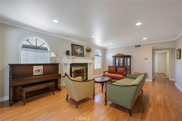 living room featuring light wood finished floors, baseboards, visible vents, a fireplace, and ornamental molding