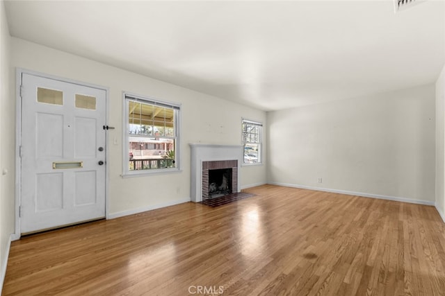 unfurnished living room with baseboards, light wood-style floors, and a brick fireplace
