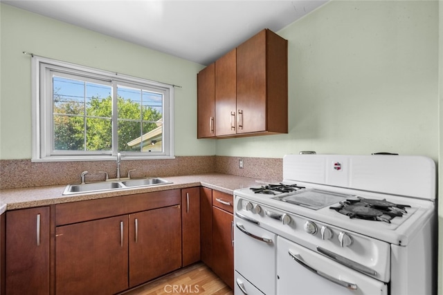 kitchen with white gas range, light countertops, a sink, and light wood-type flooring