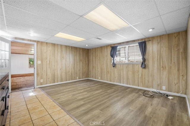 empty room featuring baseboards, wood finished floors, a drop ceiling, and wood walls