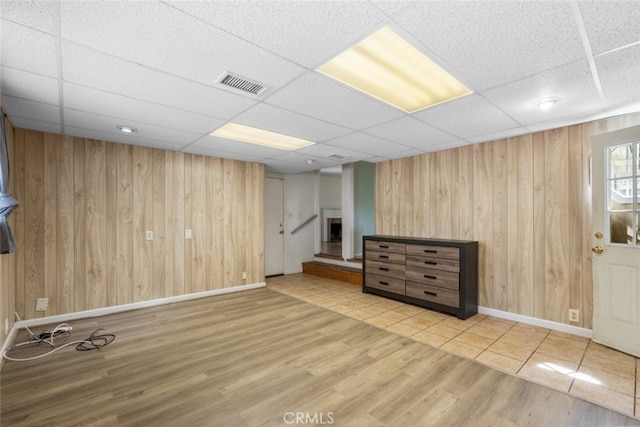 below grade area featuring a drop ceiling, wood finished floors, wooden walls, and visible vents