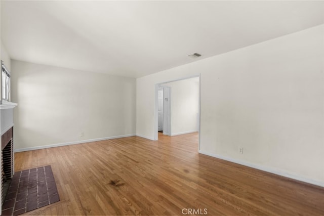 unfurnished living room with baseboards, visible vents, a tiled fireplace, and wood finished floors