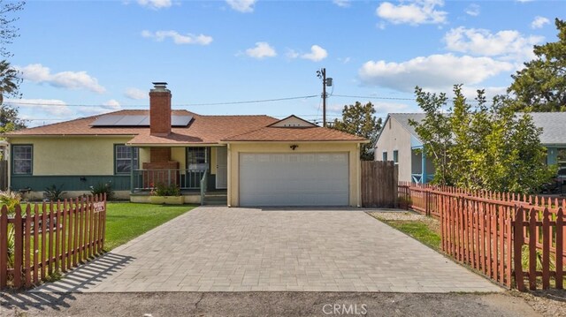 ranch-style home with fence, roof mounted solar panels, decorative driveway, a garage, and a chimney