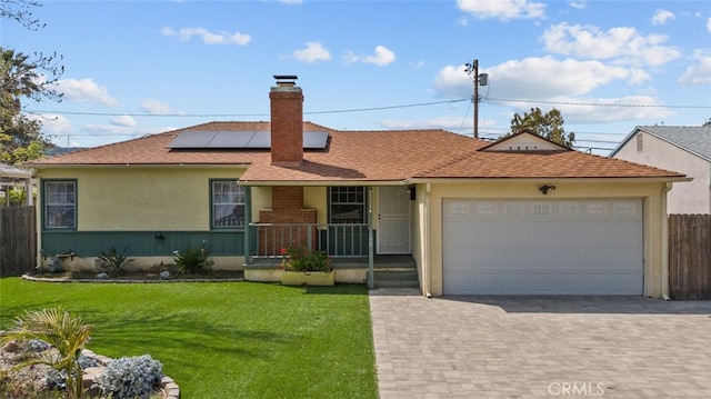 single story home featuring an attached garage, roof mounted solar panels, decorative driveway, a front lawn, and a chimney