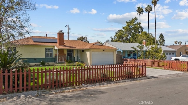 single story home featuring an attached garage, a chimney, concrete driveway, solar panels, and a fenced front yard