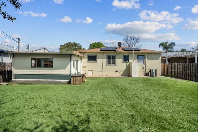 back of property with roof mounted solar panels, stucco siding, fence, and a yard