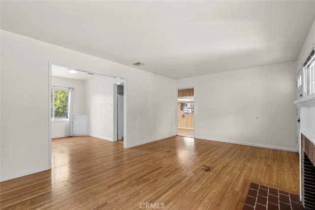 unfurnished living room featuring a fireplace with flush hearth, baseboards, visible vents, and light wood-type flooring