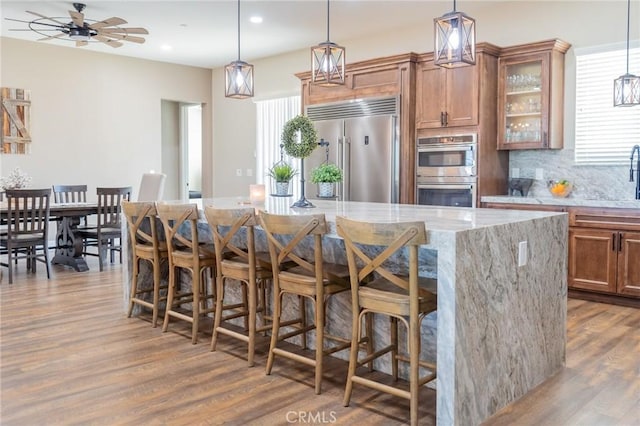 kitchen with brown cabinets, a breakfast bar, stainless steel appliances, dark wood-style flooring, and light stone countertops