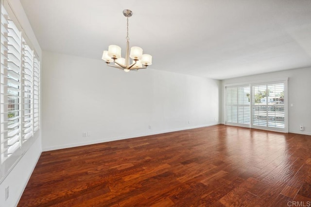 empty room with an inviting chandelier, baseboards, and wood finished floors