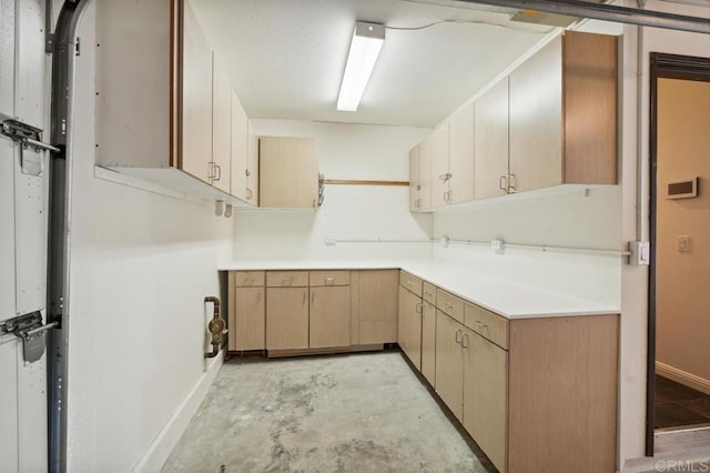 kitchen featuring baseboards, light countertops, and unfinished concrete flooring