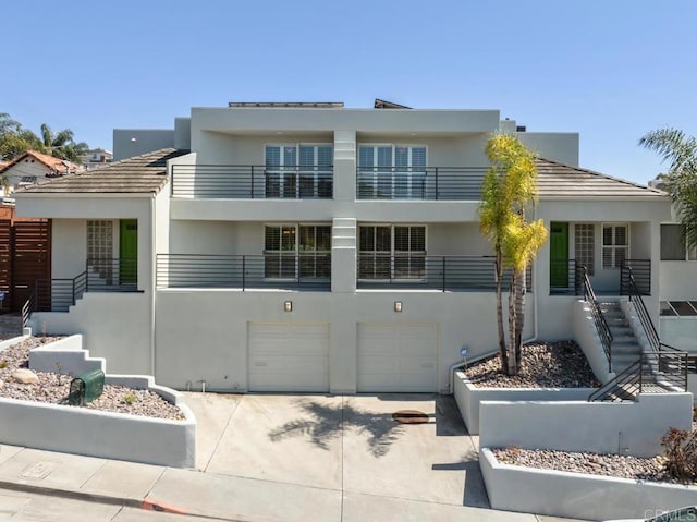 view of front facade with stairway, an attached garage, driveway, and stucco siding