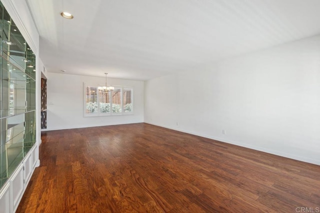 spare room featuring baseboards, wood finished floors, and a chandelier