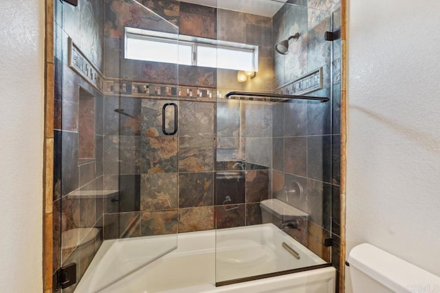 bathroom featuring toilet and shower / bath combination with glass door