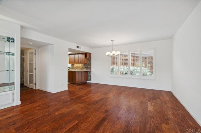 unfurnished living room with baseboards, an inviting chandelier, dark wood finished floors, and visible vents