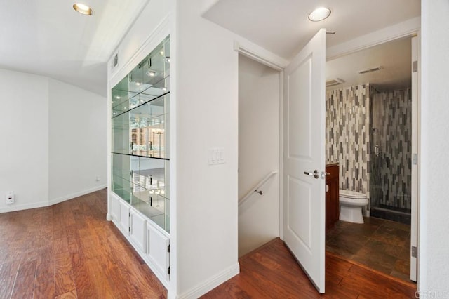 hallway with baseboards, wood finished floors, and visible vents