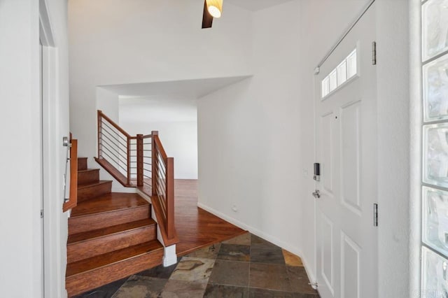 foyer entrance with baseboards, a towering ceiling, stone finish floor, and stairway