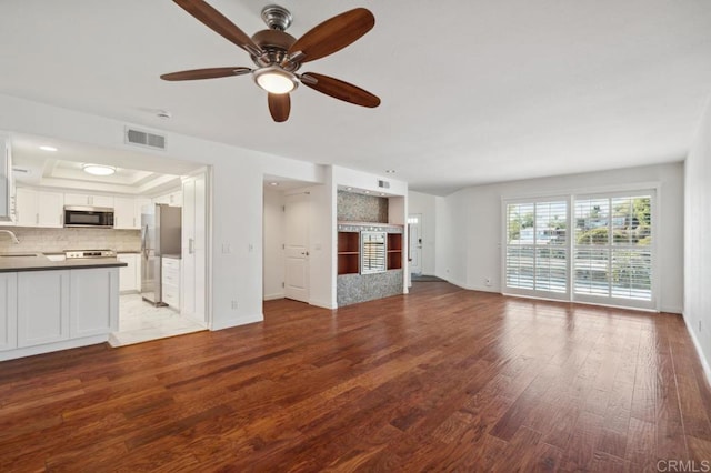 unfurnished living room with visible vents, wood finished floors, baseboards, ceiling fan, and a sink