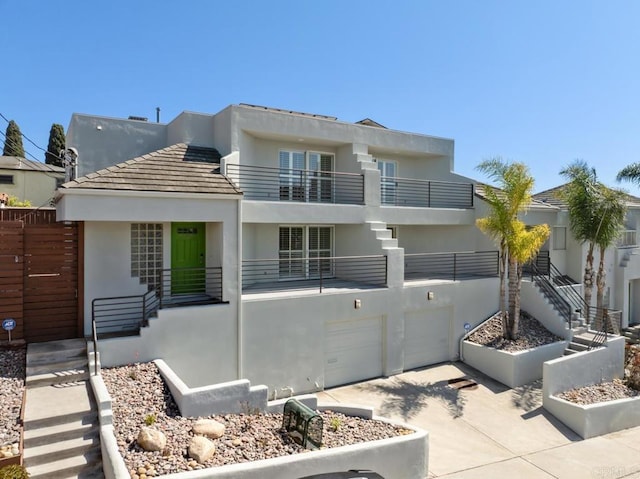 rear view of house with stairway, an attached garage, a balcony, and stucco siding