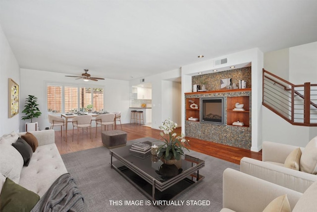 living room featuring stairs, ceiling fan, visible vents, and wood finished floors