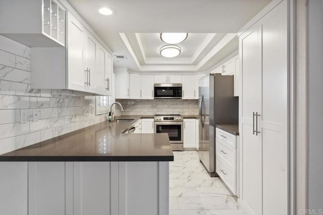 kitchen with marble finish floor, a peninsula, dark countertops, a sink, and appliances with stainless steel finishes