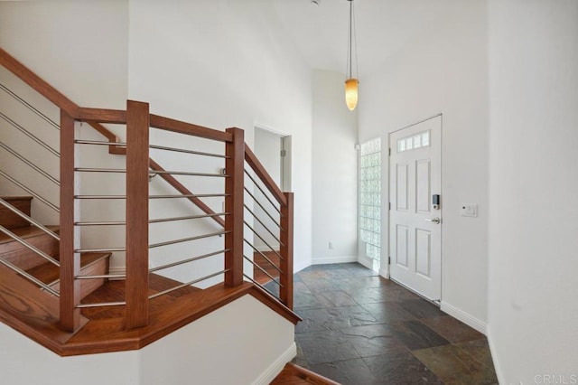 foyer with baseboards, stone tile floors, stairs, and a towering ceiling