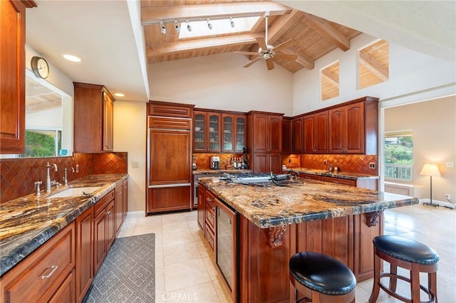 kitchen featuring a ceiling fan, a kitchen bar, beamed ceiling, paneled refrigerator, and a sink