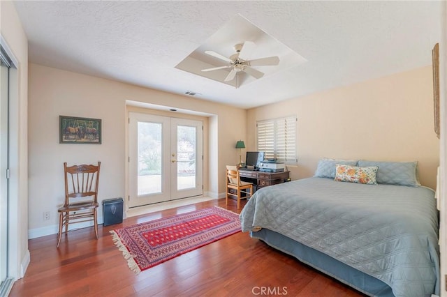 bedroom with access to outside, a tray ceiling, wood finished floors, french doors, and baseboards