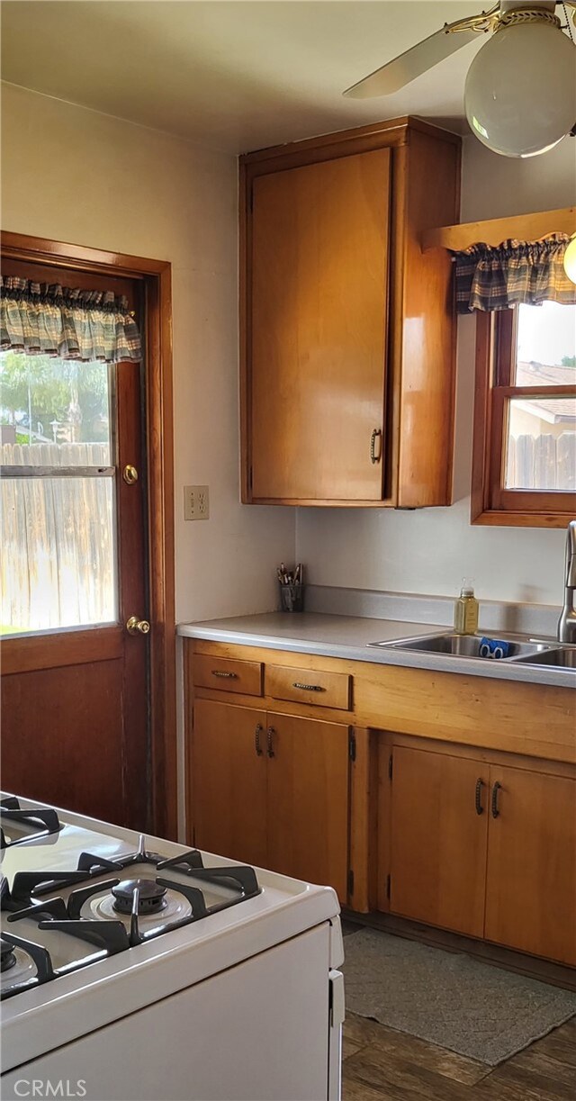 kitchen featuring brown cabinetry, light countertops, white gas stove, and a sink