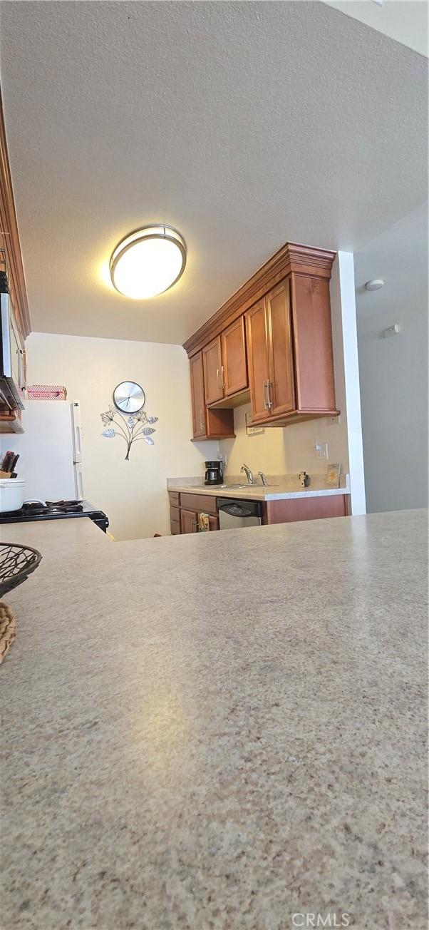 kitchen with a textured ceiling, brown cabinetry, light countertops, stainless steel microwave, and freestanding refrigerator