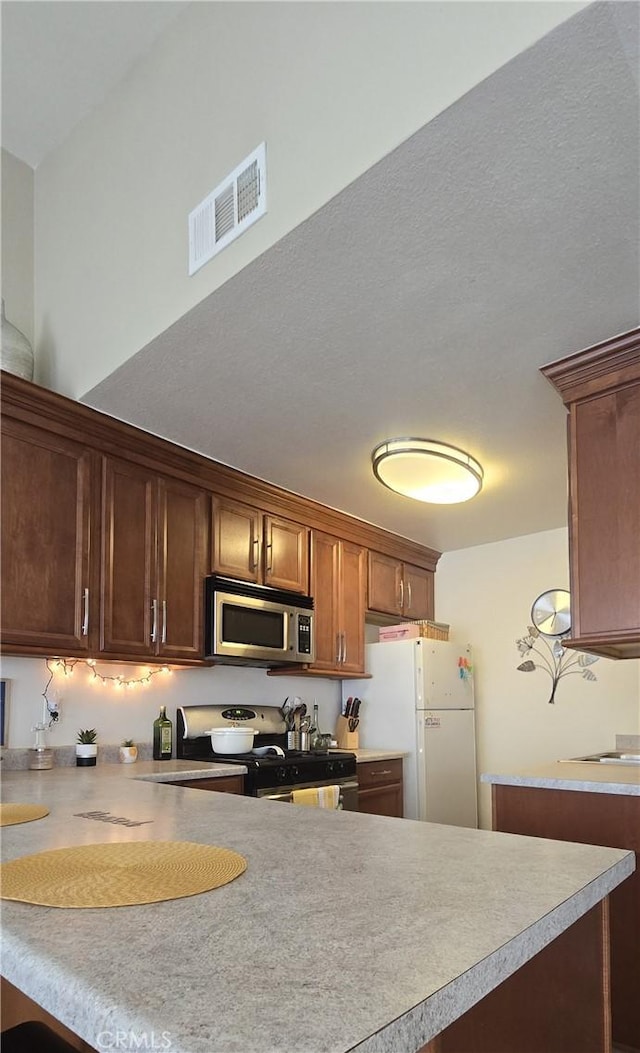 kitchen featuring a peninsula, stainless steel microwave, freestanding refrigerator, black gas range, and visible vents
