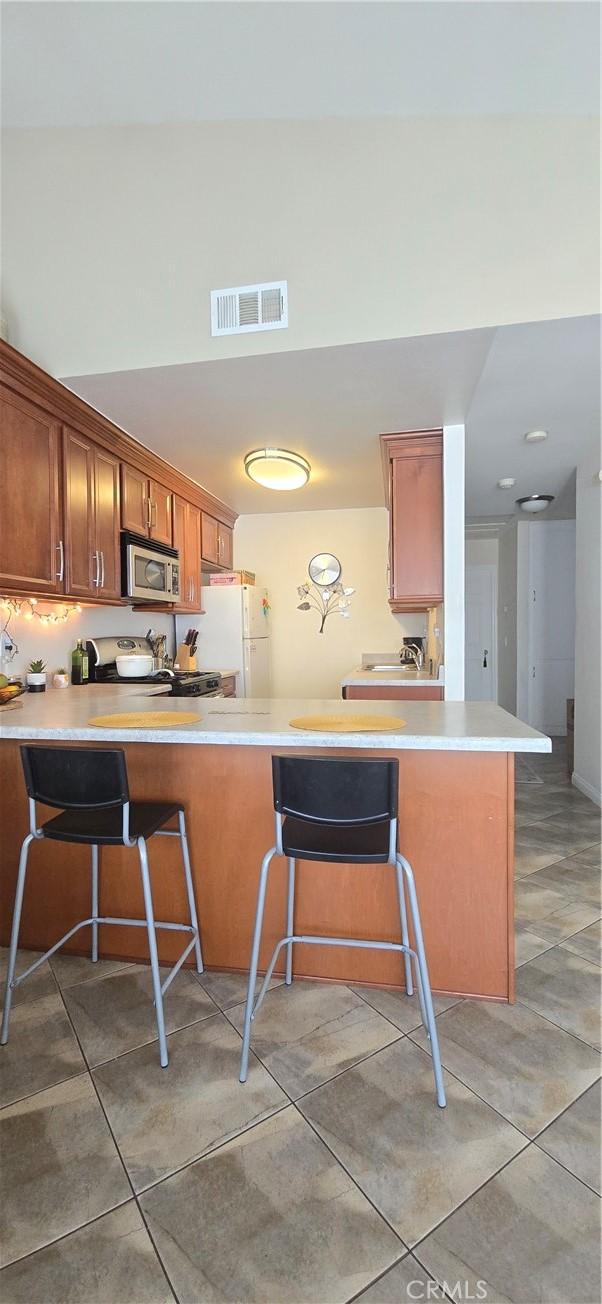 kitchen featuring stainless steel microwave, a peninsula, visible vents, and freestanding refrigerator