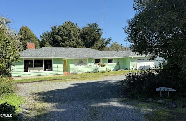 view of front of home featuring an attached garage, gravel driveway, and a chimney